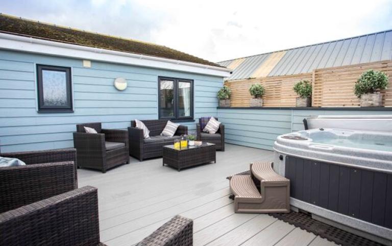 A hot tub on a deck outside a holiday home with chairs and drinks on a table