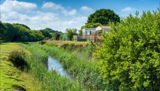 A view of a stream running through the countryside with holiday homes in the background