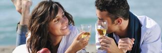 A couple drinking champagne on the beach with the sea behind their backs