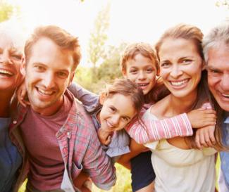 An extended family of 6 including grandparents smiling for a photo with the sun shining from the background